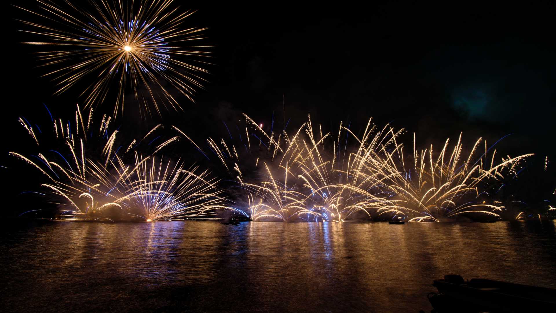 Fuegos artificiales reflejados en el agua por la noche.