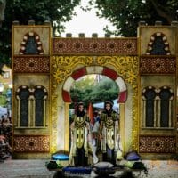 Desfile en Dénia con trajes medievales y arco decorado.