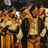 Hombres con vestidos árabes tradicionales en desfile nocturno.