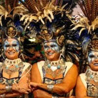 Mujeres en disfraces con plumas y maquillaje colorido.