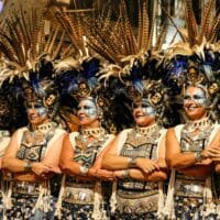 Mujeres en desfile con trajes tradicionales y plumas.