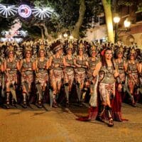 Desfile de personas con trajes tribales en festival nocturno.