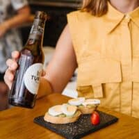 Persona con cerveza y tapas en la mesa.