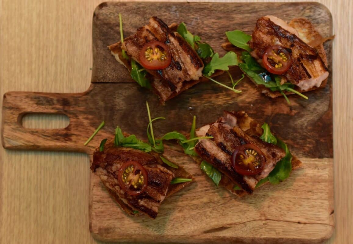 Tostas con tomate cherry y panceta en tabla de madera.