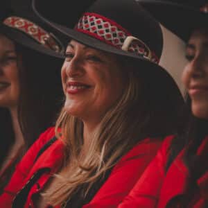 Mujeres con sombreros folklóricos y blusas rojas sonrientes.
