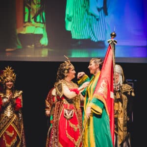 Personas en trajes medievales coloridos interactuando en el escenario.