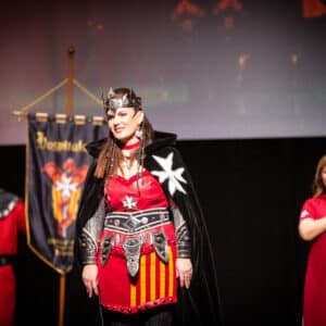 Desfile de trajes medievales en escenario con estandarte.