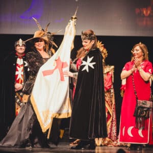 Personas con disfraces medievales y banderas en escenario.