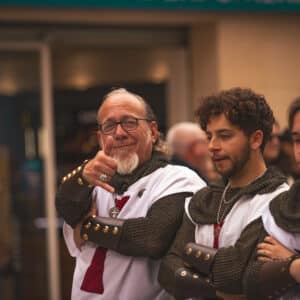 Hombres medievales en una calle, uno sonriendo.