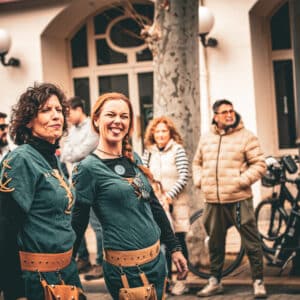 Personas en desfile festivo con trajes medievales verdes.