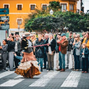 Persona vestida de flamenco cruza calle ante público