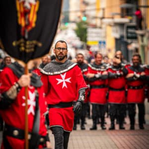 Desfile de hombres con trajes medievales rojos.