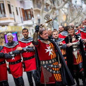Grupo de personas en desfile medieval, trajes rojos y negros.