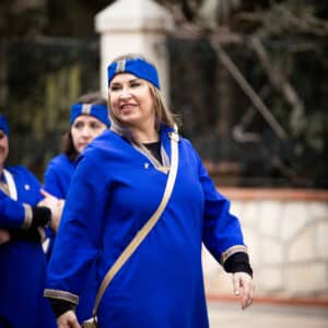 Mujer sonriendo vestida de azul en desfile cultural.