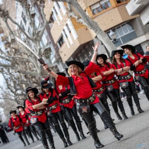 Desfile festivo con trajes rojos y sombreros negros.