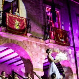 Bailarina elevada en escenario iluminado con luces moradas.