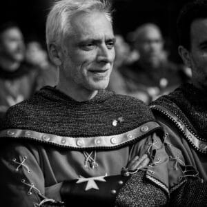 Hombre sonriente en traje medieval, blanco y negro.