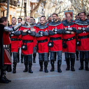 Desfile medieval de hombres con trajes rojos y negros.