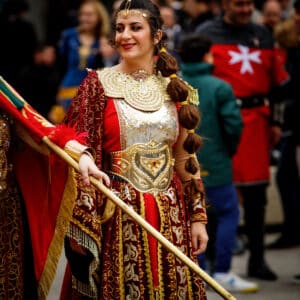 Mujer con traje medieval decorado, llevando bandera. Fiesta.