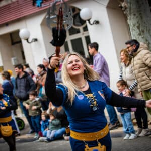 Desfile festivo con mujer sonriente y público alrededor.