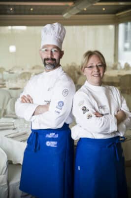 Dos chefs con uniformes blancos y delantales azules.