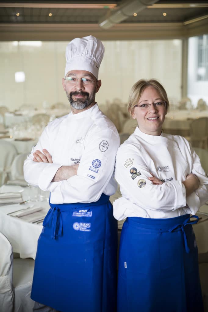 Dos chefs con uniformes blancos y delantales azules.