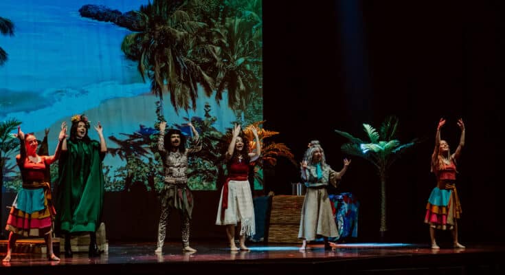 Actores actuando en un escenario con fondo de playa.