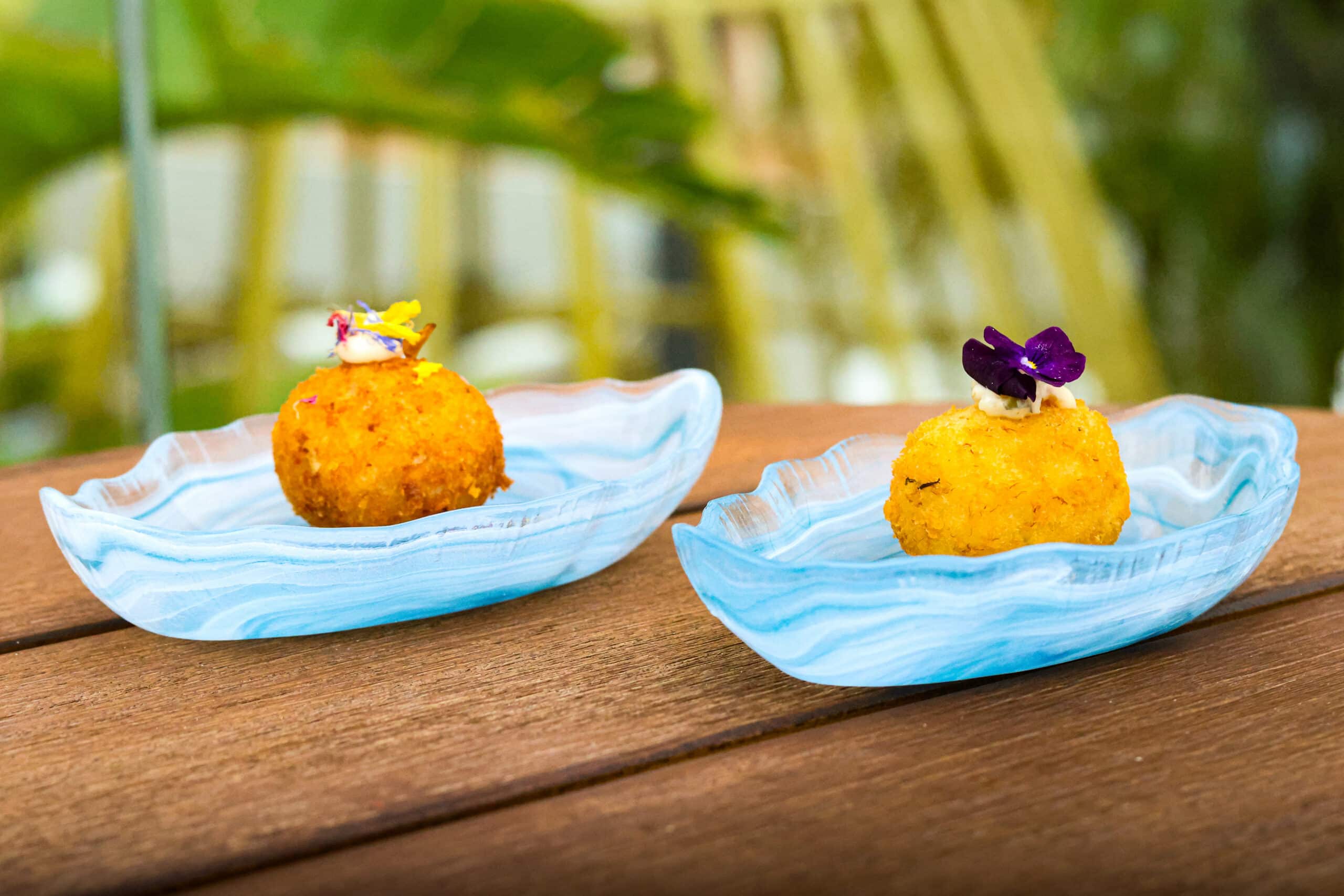 Dos croquetas gourmet con flores comestibles en platos azules