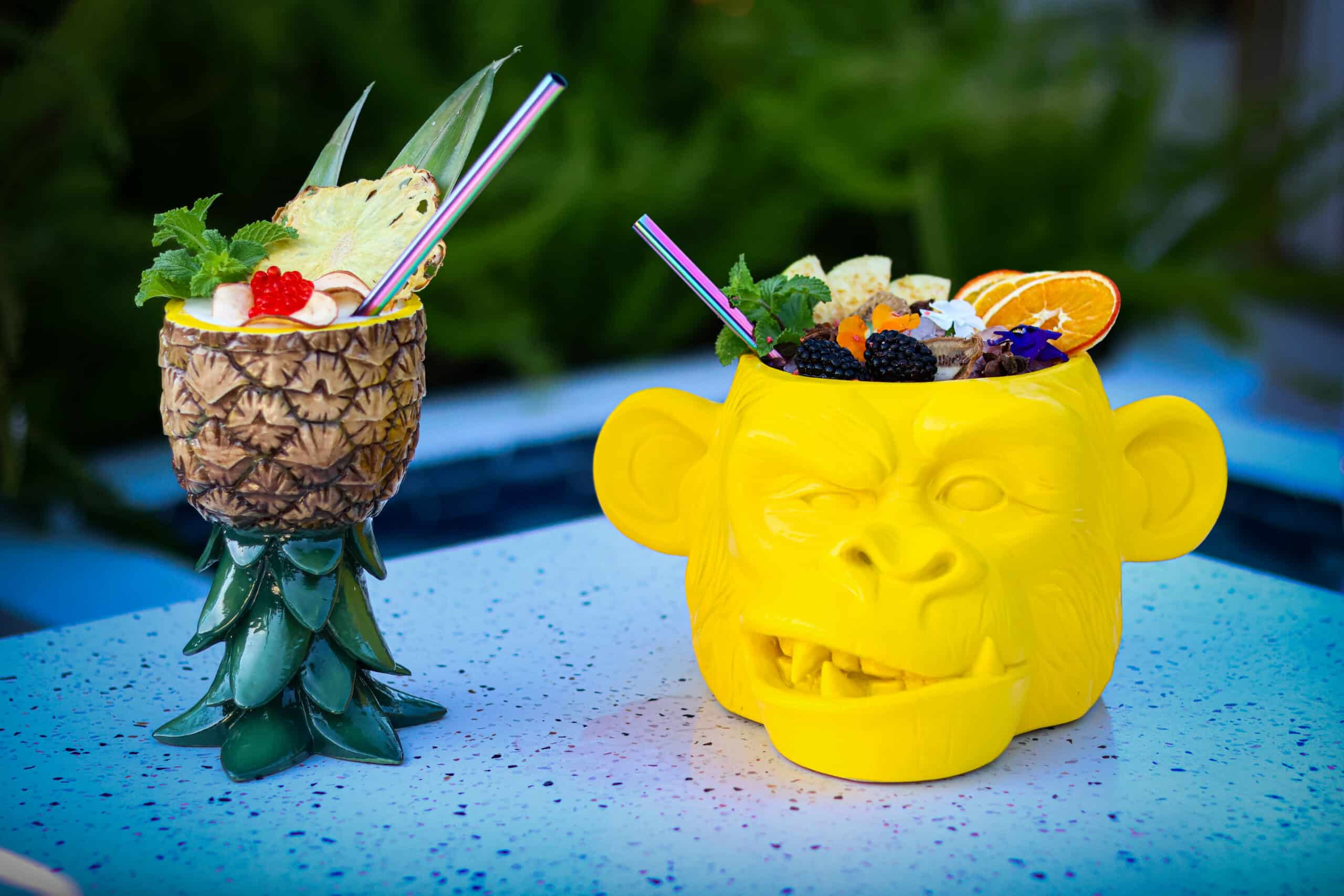 Dos cócteles tropicales en copas decorativas de piña y mono